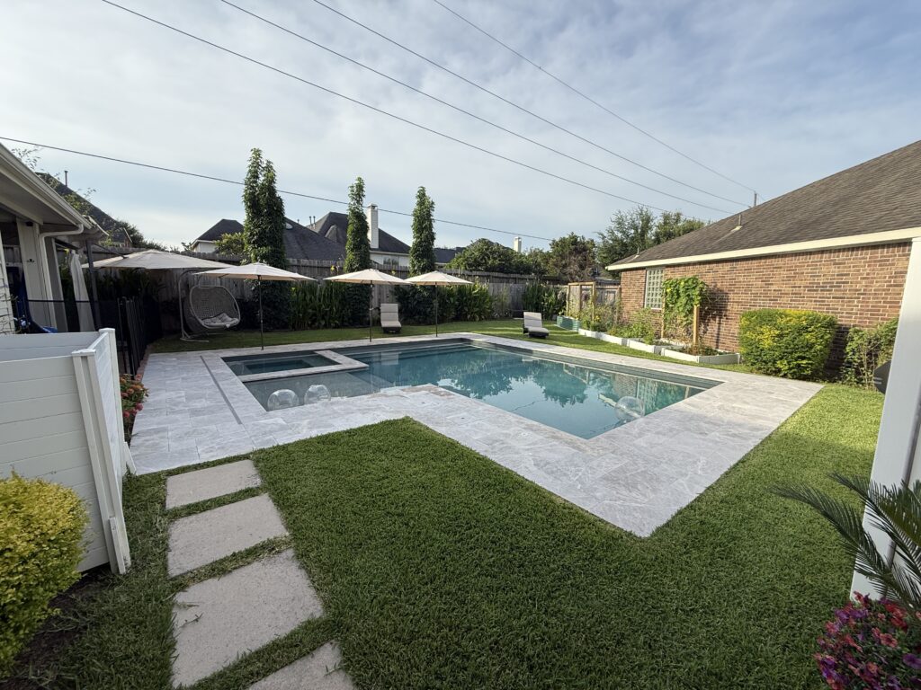 Backyard with a rectangular pool, stone deck, and several white umbrellas overlooking a fenced yard.