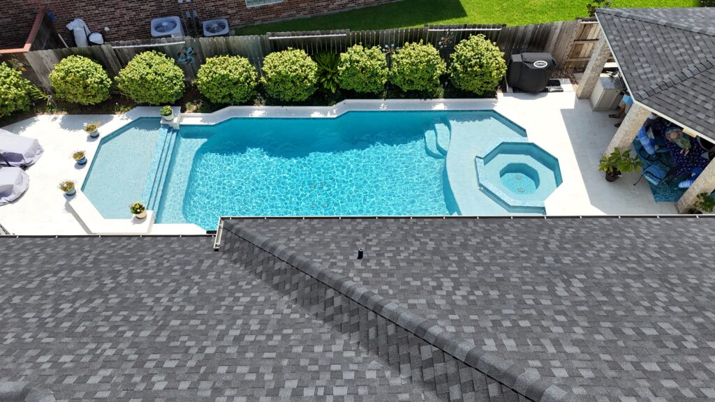 Aerial view of a rectangular swimming pool with a separate spa, surrounded by a white deck and trimmed hedges along a wooden fence.