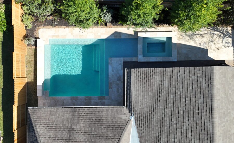 Aerial view of a modern backyard with a turquoise rectangular pool, built-in steps, and a square spa alcove surrounded by a stone patio and greenery.