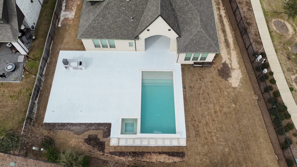Aerial view of a modern home with a rectangular white patio and a turquoise in-ground pool.