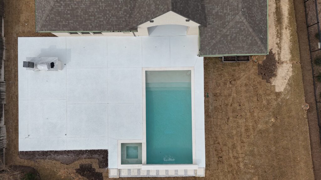 Aerial view of a modern house with a large white deck surrounding a rectangular turquoise pool.