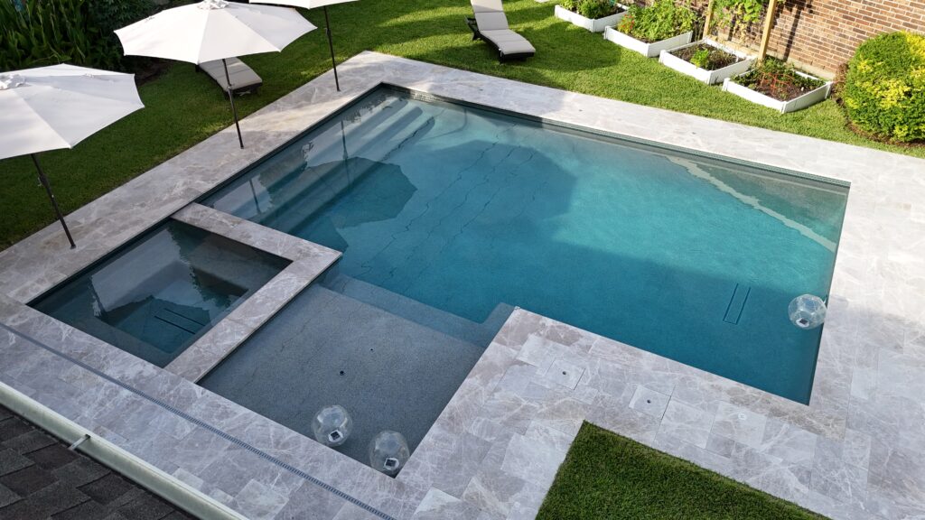 Aerial view of a rectangular pool with a built‑in spa, surrounded by light stone decking and white sun umbrellas.