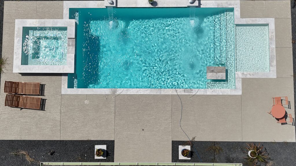 Aerial drone view of a custom rectangular pool and raised spa with tanning ledge, wide concrete coping, and decorative gravel border — completed by Beach'n Pools in Cane Island, Katy TX