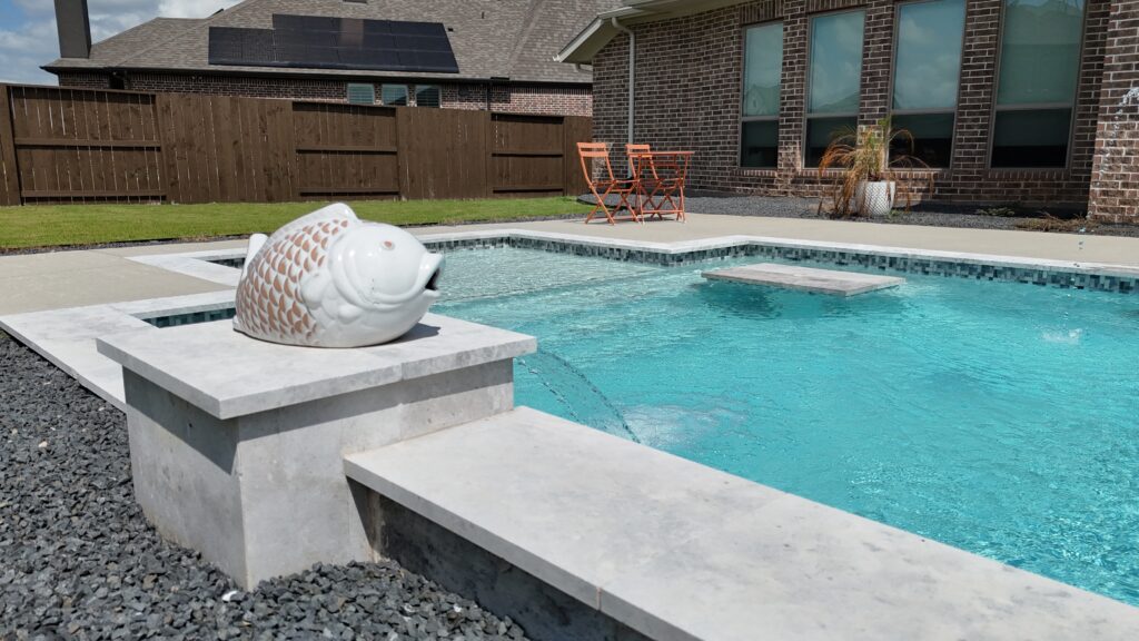 Aerial drone view of a custom rectangular pool and raised spa with tanning ledge, wide concrete coping, and decorative gravel border — completed by Beach'n Pools in Cane Island, Katy TX