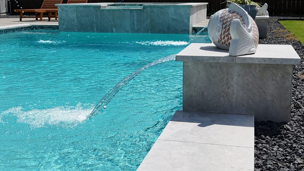 Aerial drone view of a custom rectangular pool and raised spa with tanning ledge, wide concrete coping, and decorative gravel border — completed by Beach'n Pools in Cane Island, Katy TX