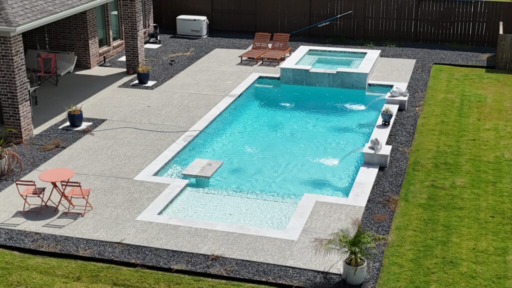 Aerial drone view of a custom rectangular pool and raised spa with tanning ledge, wide concrete coping, and decorative gravel border — completed by Beach'n Pools in Cane Island, Katy TX
