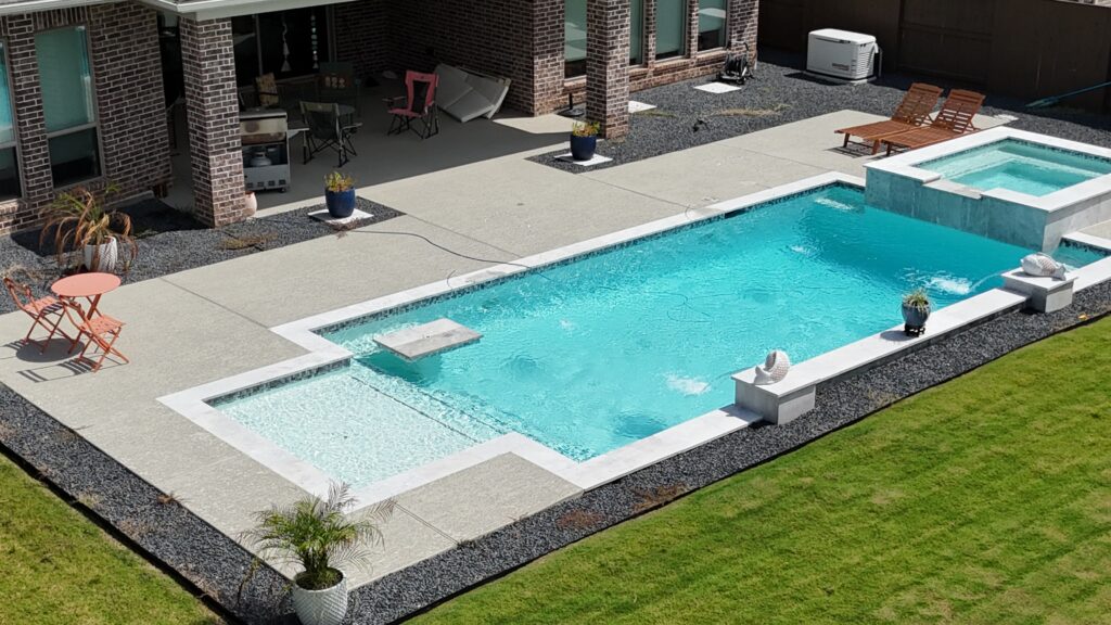 Aerial drone view of a custom rectangular pool and raised spa with tanning ledge, wide concrete coping, and decorative gravel border — completed by Beach'n Pools in Cane Island, Katy TX